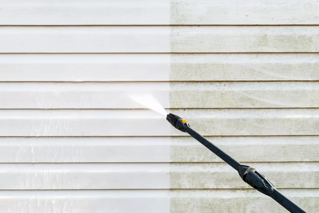 Power rinsing the exterior of a house, with white painted siding