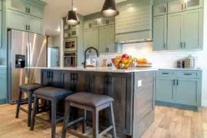 A newly painted kitchen with sage green cabinets, bright lights, and hardwood floors