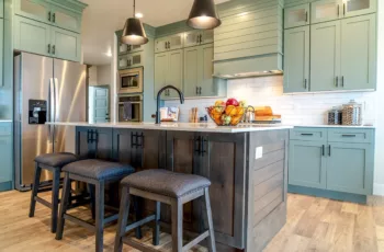 A newly painted kitchen with sage green cabinets, bright lights, and hardwood floors