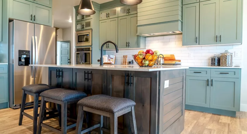 A newly painted kitchen with sage green cabinets, bright lights, and hardwood floors