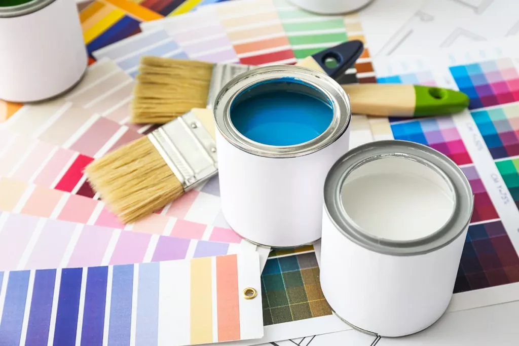 A selection of paint cans and paint color samples on the floor next to some brushes