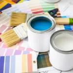 A selection of paint cans and paint color samples on the floor next to some brushes