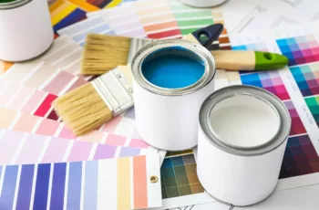 A selection of paint cans and paint color samples on the floor next to some brushes