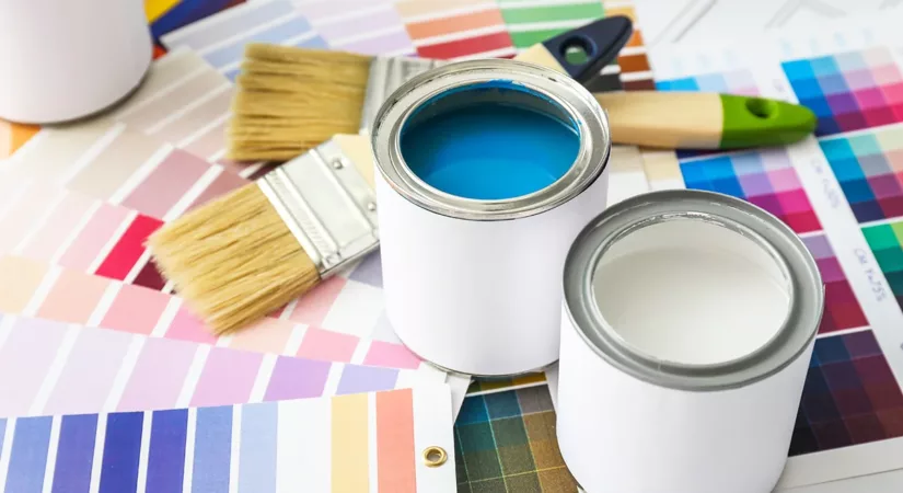 A selection of paint cans and paint color samples on the floor next to some brushes