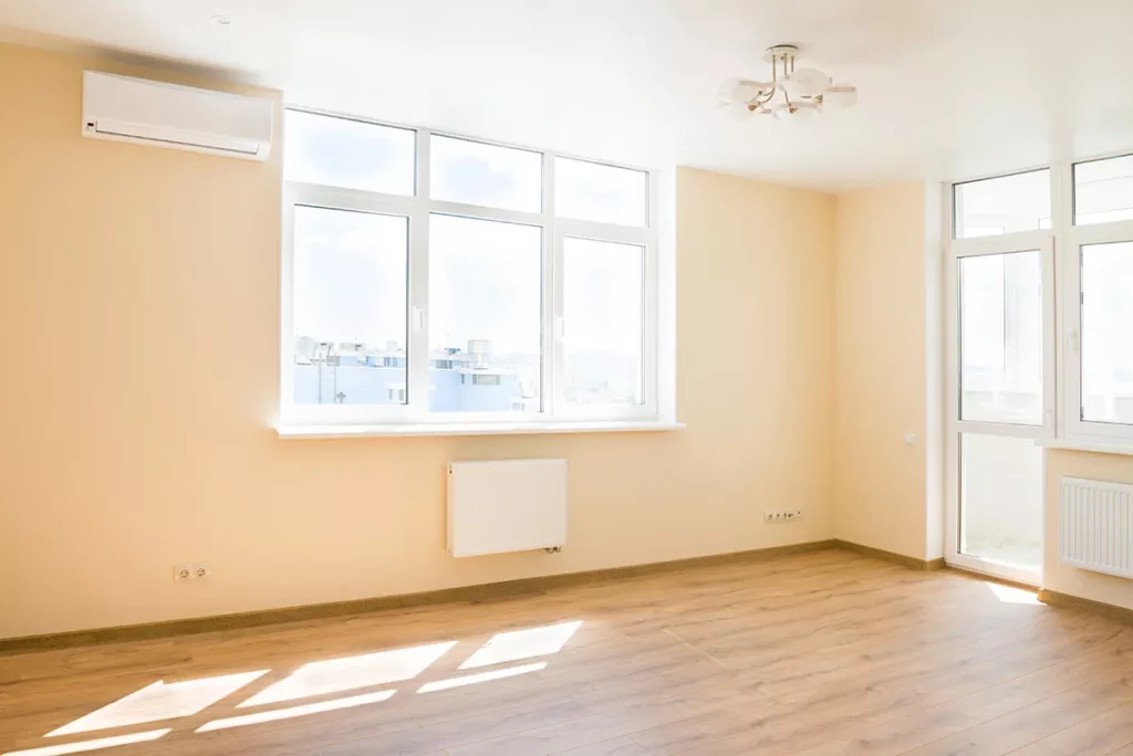 An empty living room with bright windows and walls painted a soft pastel yellow