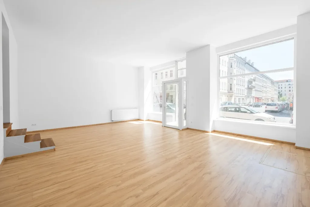 The interior of an empty retail or office space with large windows and newly painted white walls